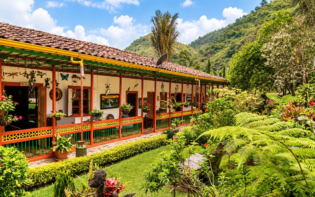 Corredor de una hacienda cafetera con tejas, pilares rojos y jardín, al pie de la montaña