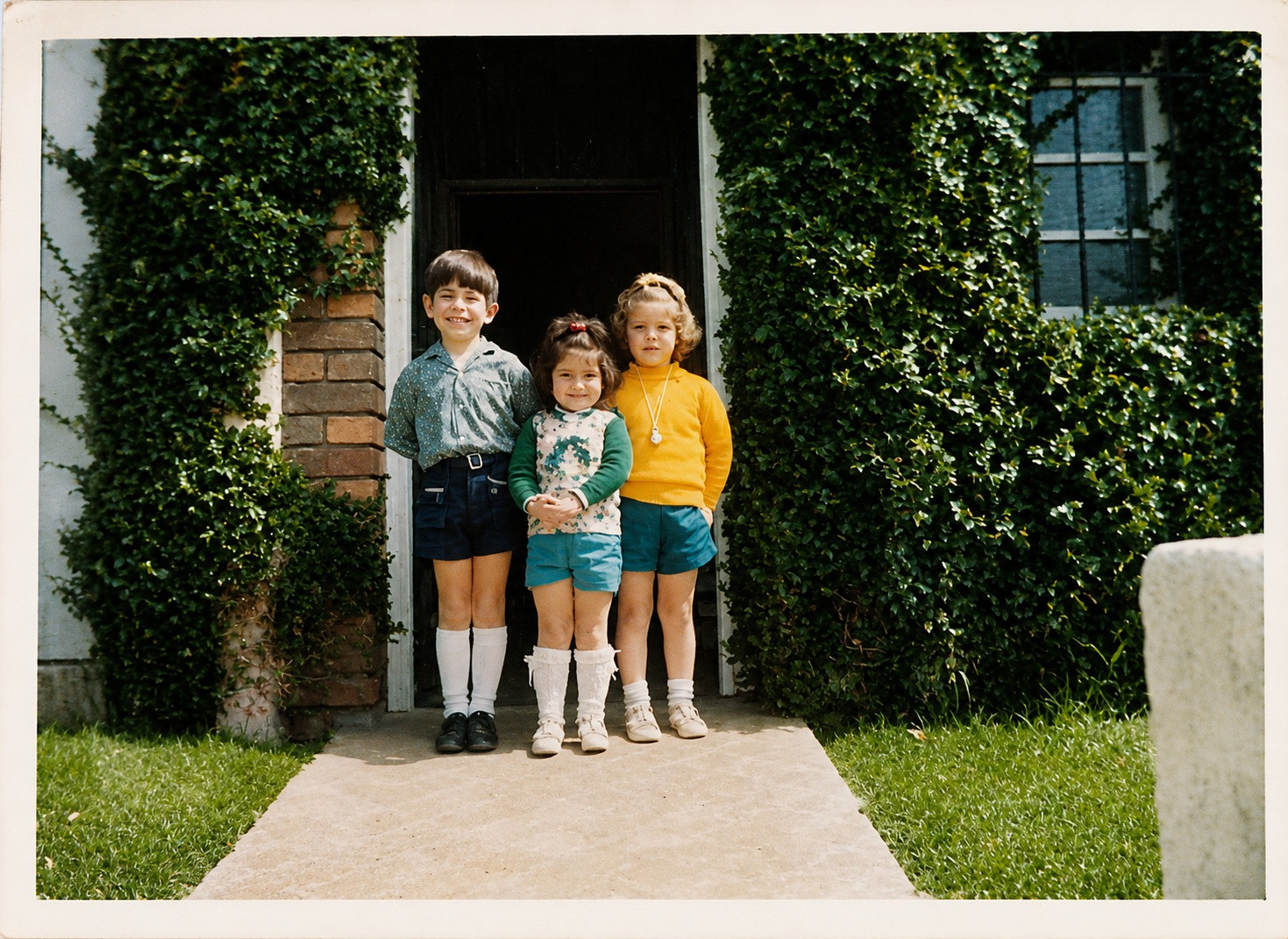 Los tres hermanos en la entrada de la casa, con la enredadera verde cubriendo el arco del portal